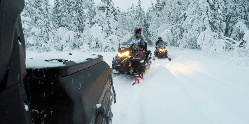 Mensen op sneeuwscooters rijden door het besneeuwde landschap van Zweeds Lapland