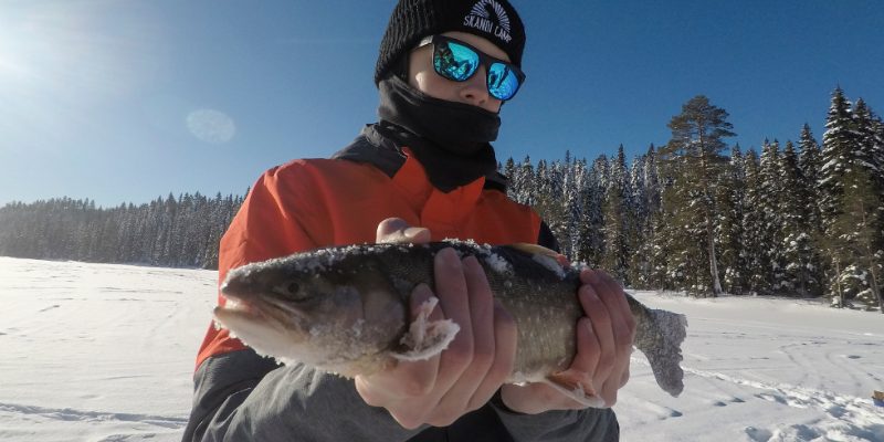 Man met zonnebril staat op een bevroren meer met vis in zijn handen in Zweeds Lapland